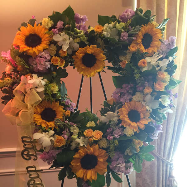 Heart-shaped floral wreath with sunflowers and pastel blooms on an easel