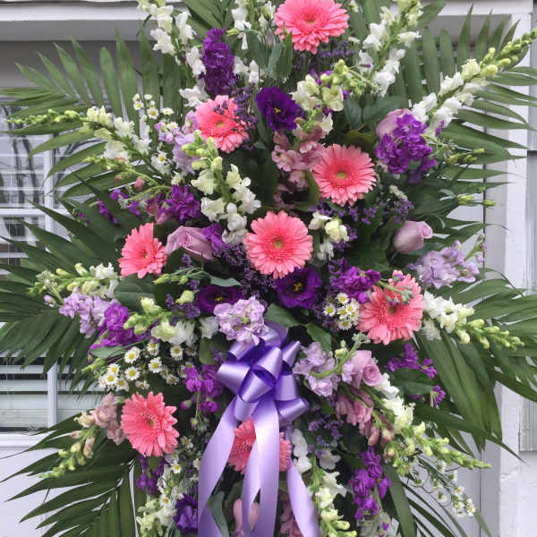 Standing floral spray with pink gerberas, purple blooms, and a lavender ribbon