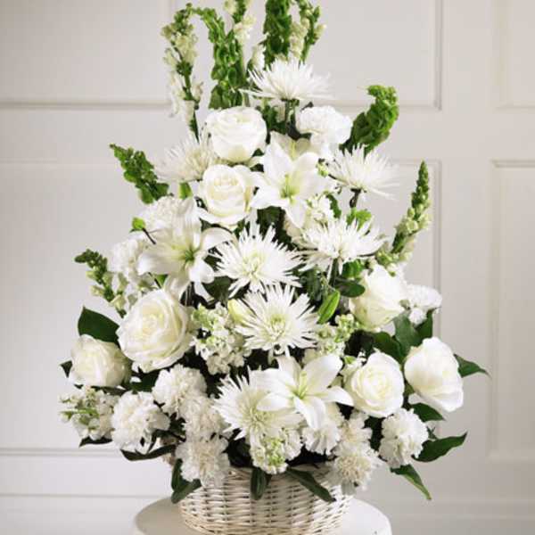 White floral arrangement in a wicker basket with roses, lilies, and spiky blooms