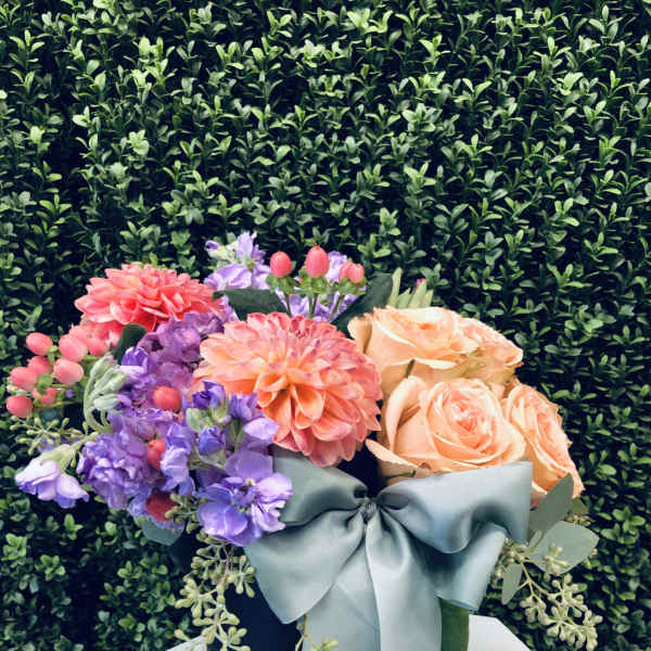 Bouquet of peach roses, purple blooms, and coral dahlias in a black hat box with a blue ribbon.