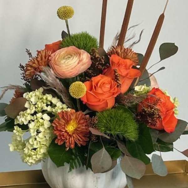 Orange roses and mixed blooms in a white pumpkin vase