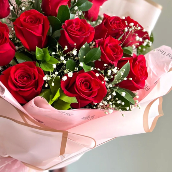 Bouquet of red roses with white filler flowers wrapped in pink paper