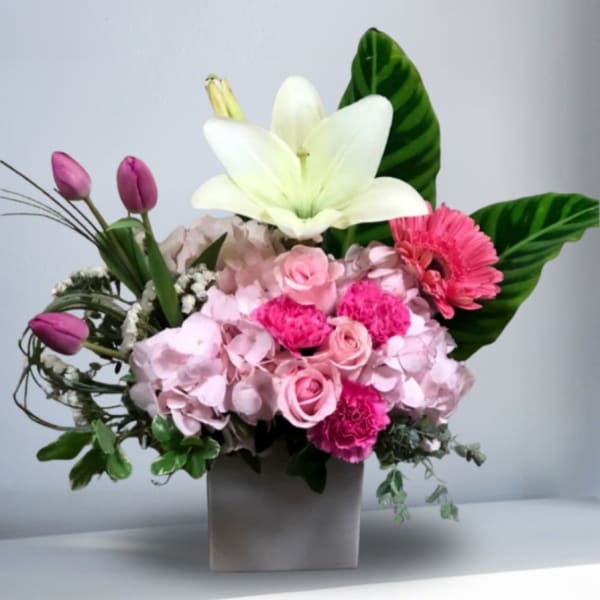 Pink floral arrangement with a white lily in a square vase