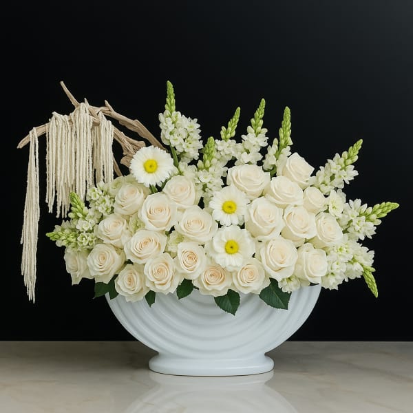 White roses and daisy-like flowers in a white vase with macramé tassels