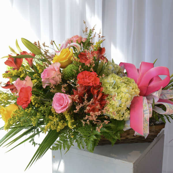 Colorful mixed flower arrangement in a basket with pink ribbon