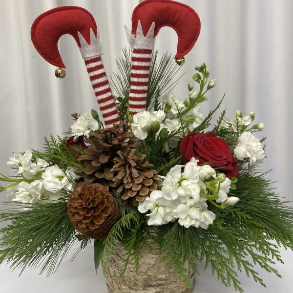 Holiday floral arrangement with red roses, white blooms, pinecones, and elf decorations