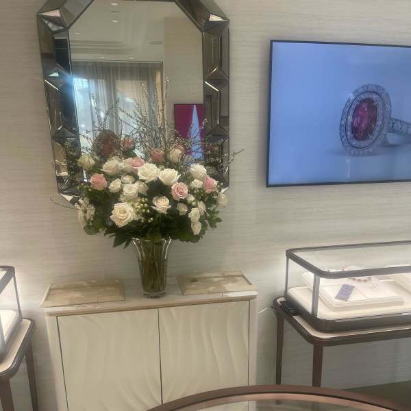 Tall arrangement of white and pale pink roses in a clear glass vase beneath a wall mirror