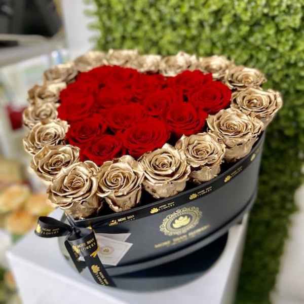 Round black hatbox of red and gold roses with red blooms shaped into a heart.