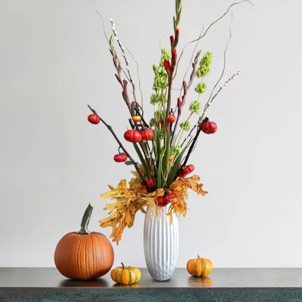 Tall autumn arrangement in a white vase with pumpkins and fall leaves