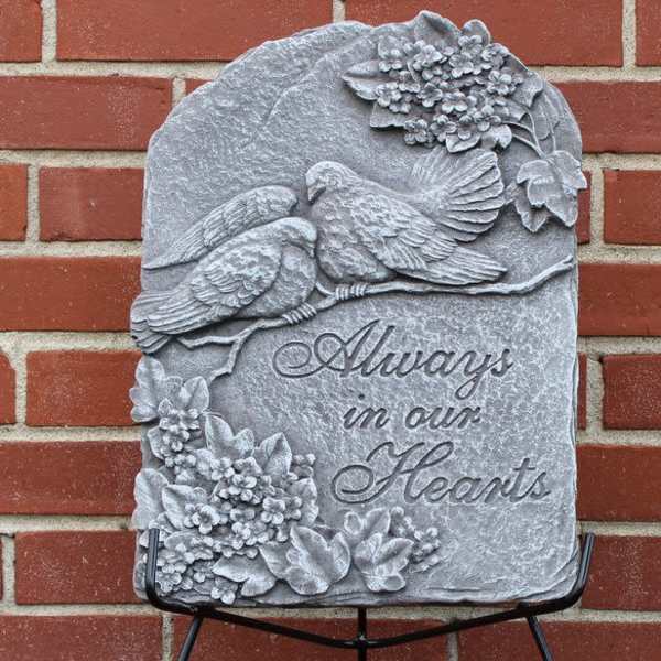 Gray memorial plaque with two birds and floral reliefs against a brick wall
