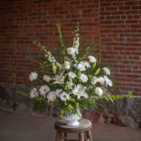 White floral arrangement in a white vase with a green ribbon