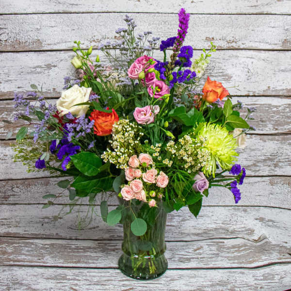 Mixed bouquet of roses, chrysanthemums, and purple filler flowers in a glass vase