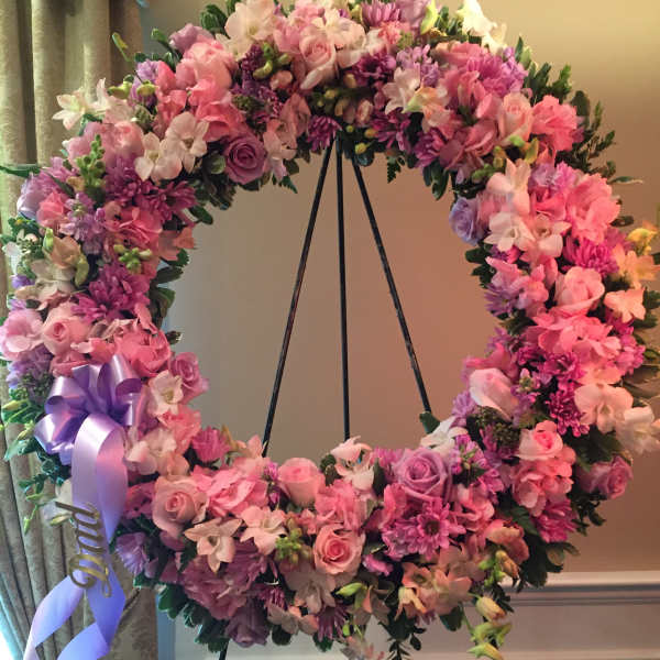 Pink and purple floral wreath on a black stand with a lavender ribbon