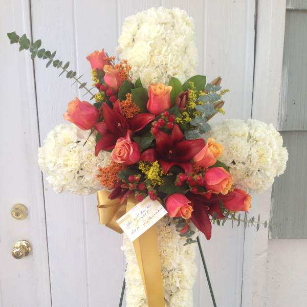 Cross-shaped floral spray with white flowers, red roses, and a gold ribbon