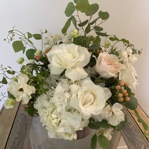 White roses and hydrangeas arranged in a vase with greenery and peach berries.