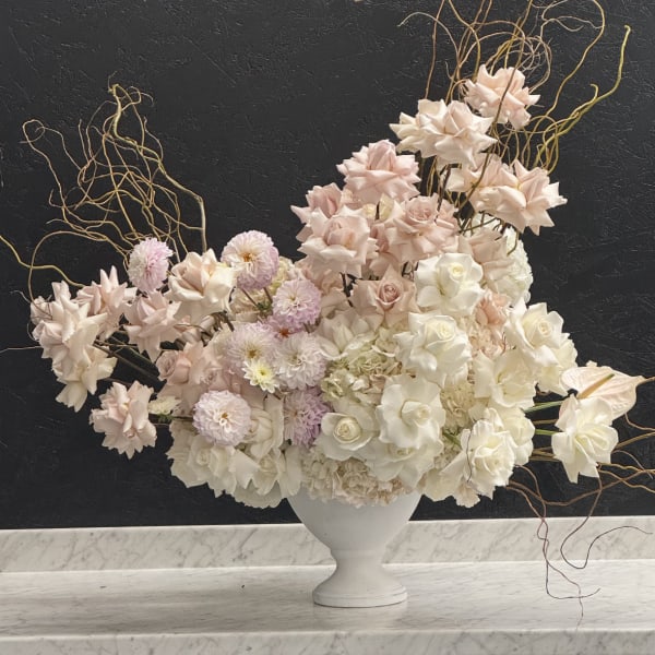 Large asymmetrical arrangement of blush and white flowers in a white urn