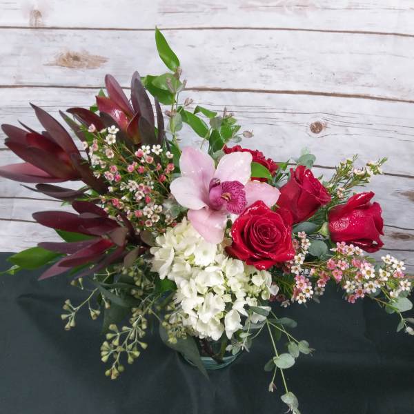 Bouquet of red roses, pink orchid, and white hydrangea in a glass vase