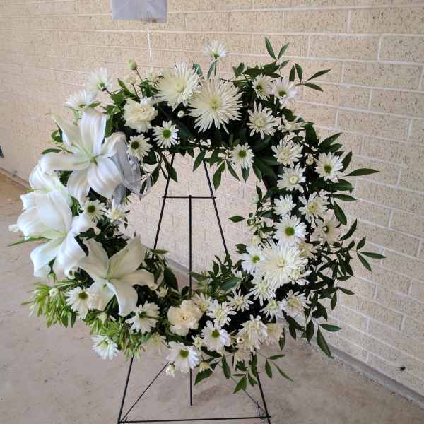 White floral wreath on a black stand with lilies and daisies