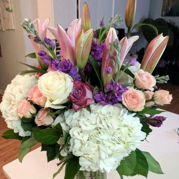 Bouquet of pink lilies, roses, hydrangeas, and purple flowers in a glass vase