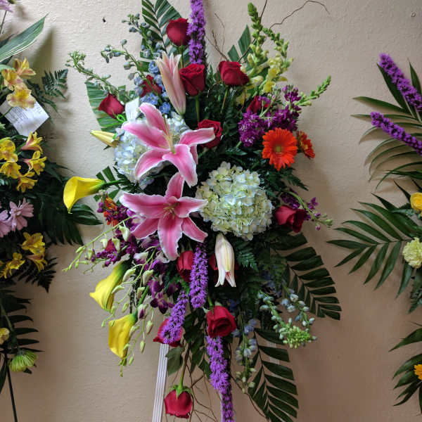 Tall standing floral spray with pink lilies, red roses, and purple accents