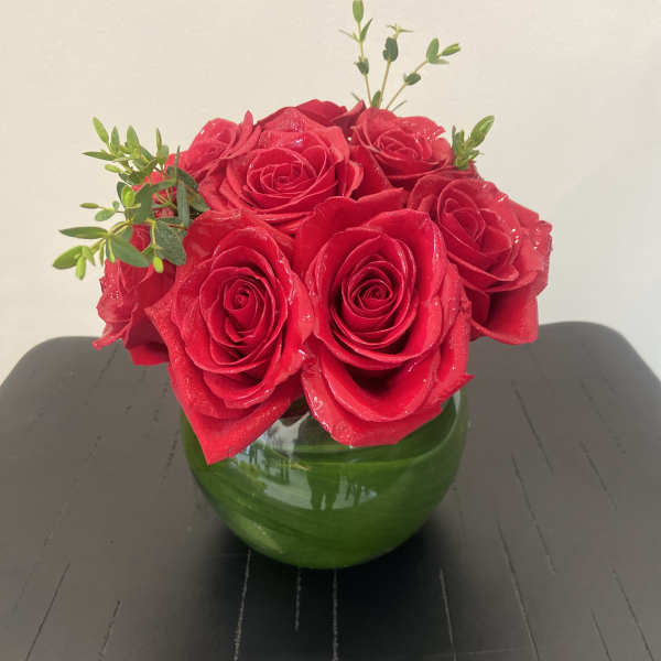 Red roses arranged in a green glass vase