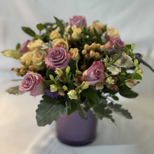 Lavender and cream rose bouquet in a purple vase