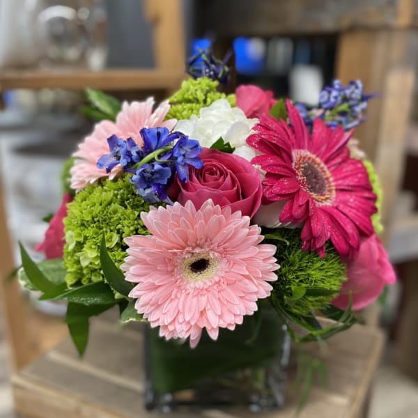 Mixed bouquet with pink gerbera daisies, roses, and blue flowers in a glass vase