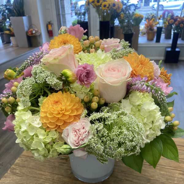 Mixed pastel bouquet in a gray vase with roses, hydrangeas, and orange blooms