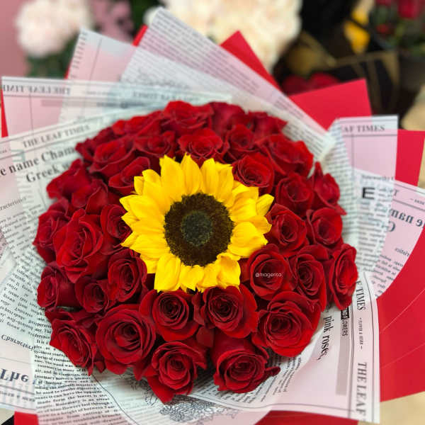 Red rose bouquet with a yellow sunflower center wrapped in newspaper-style paper