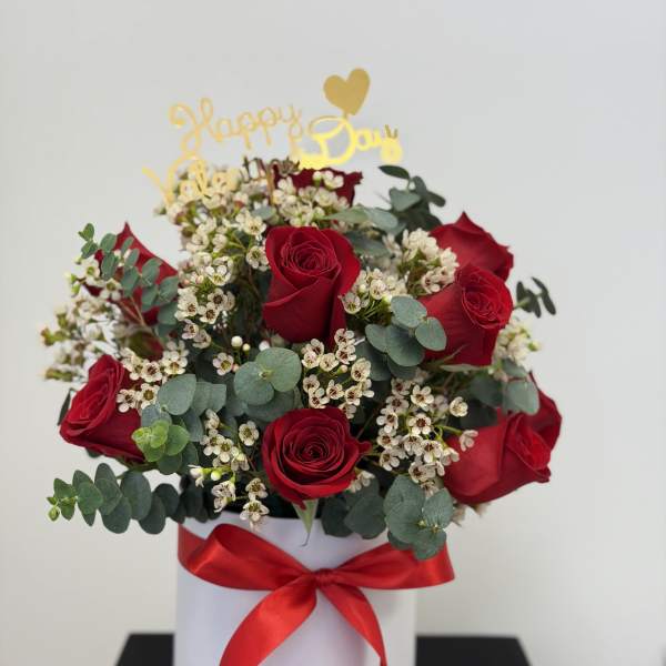 Red roses and white filler flowers in a white hat box with a red ribbon