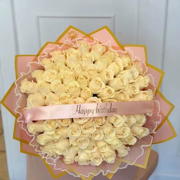 Bouquet of cream roses wrapped in pink paper with a Happy birthday ribbon