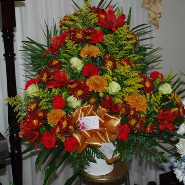 Large red and orange floral arrangement with a gold bow in a white vase