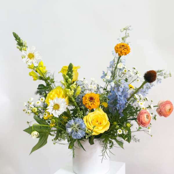 Mixed bouquet in a white vase with yellow, blue, and white flowers