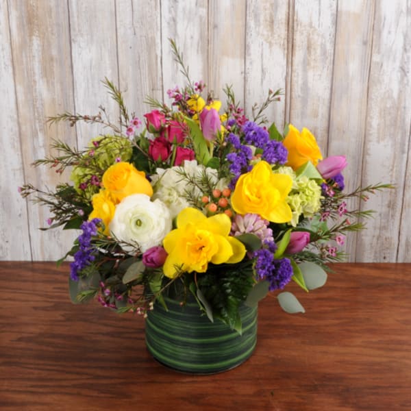 Low arrangement of yellow, purple, pink, and white flowers in a green striped vase