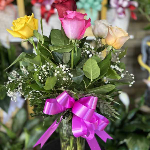 Bouquet of multicolored roses in a glass vase with a pink ribbon