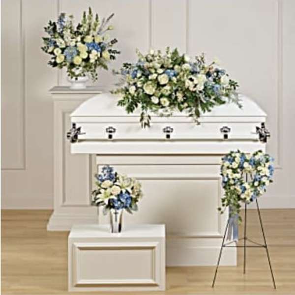 White casket with blue and white floral sprays in a funeral room