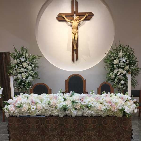 White floral altar arrangement beneath a crucifix in a church