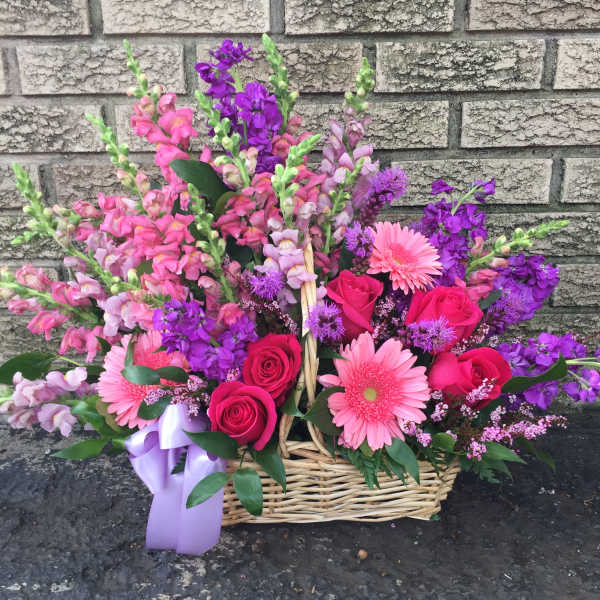 Basket arrangement of pink and purple flowers with roses and gerbera daisies