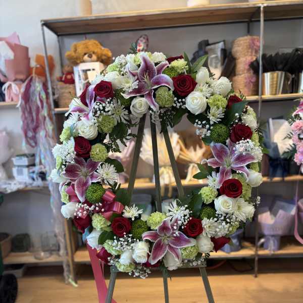 Circular floral wreath on an easel with red, white, and pink blooms