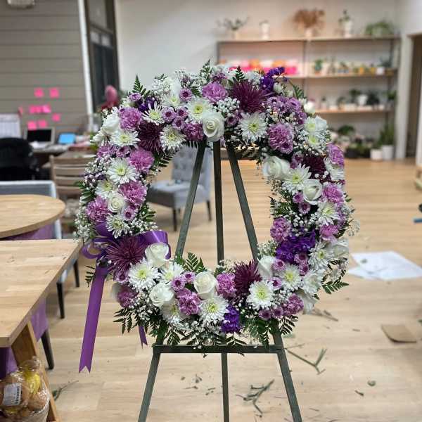 Purple and white floral wreath on an easel with a ribbon