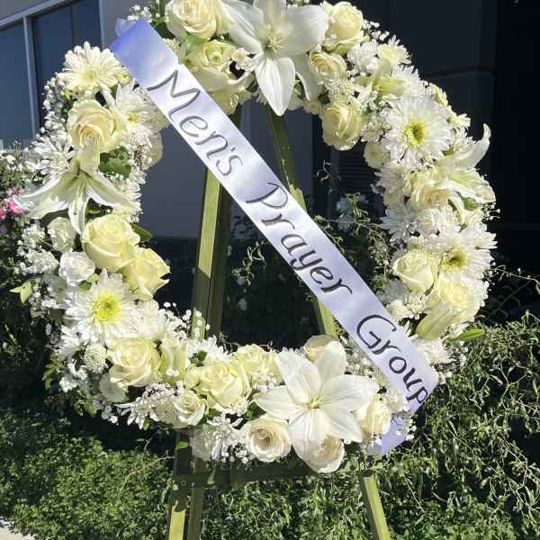 White floral funeral wreath on an easel with a memorial ribbon