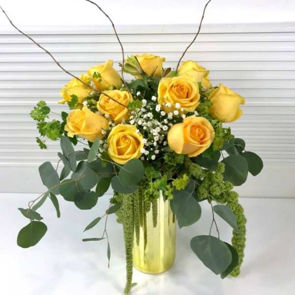 Yellow roses in a gold vase with trailing greenery