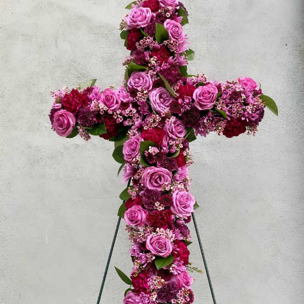 Standing floral cross of pink and burgundy blooms on a metal easel.