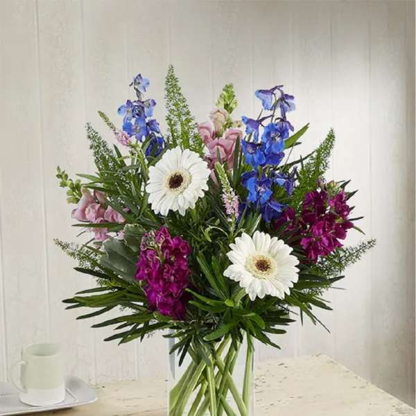 Mixed bouquet with white daisies, blue and pink flowers in a clear glass vase