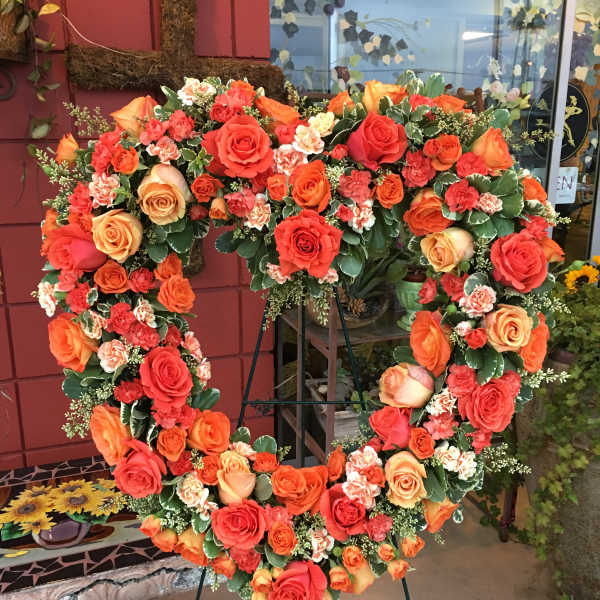 Heart-shaped floral wreath of orange and red roses on a stand