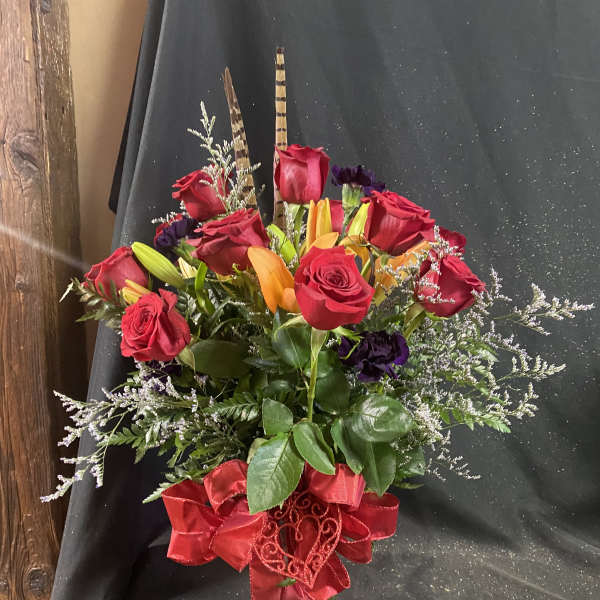 Red roses and orange lilies in a glass vase with a red ribbon