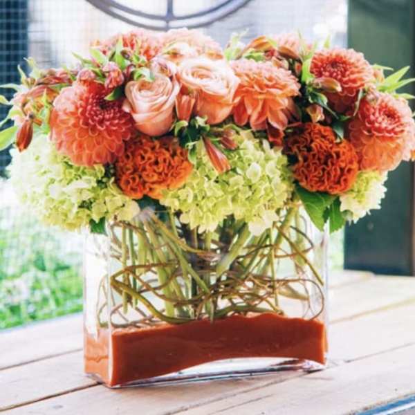 Orange and peach floral arrangement in a clear rectangular vase