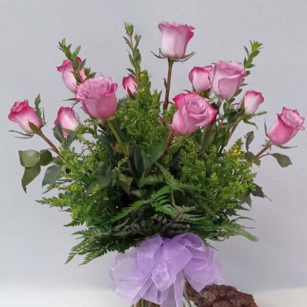 Pink roses in a glass vase with a lavender ribbon bow