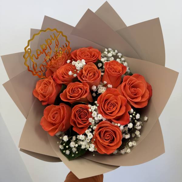 Orange roses with baby's breath in tan wrapping and a "happy birthday" topper