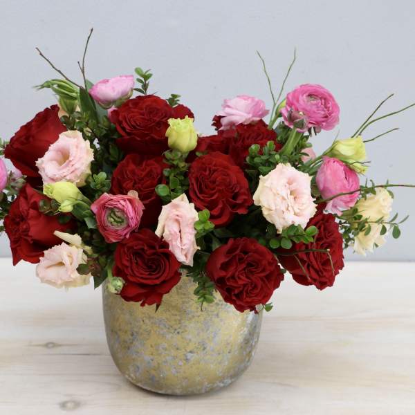 Low arrangement of red roses and pink blooms in a rustic gold-toned pot